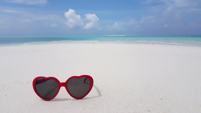 Pair of heart shaped red sunglasses sitting on the beach with the background blurred out on an exotic island in Bora Bora