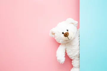 Foto auf Glas Smiling white teddy bear looking behind pastel blue wall. Mock up for happy, positive idea. Empty place for inspiration, emotional, sentimental text, quote or sayings on pink background. Front view. © fotoduets