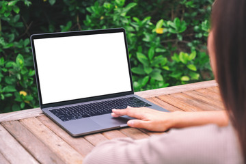 Mockup image of a woman using and touching on laptop touchpad with blank white desktop screen on wooden table