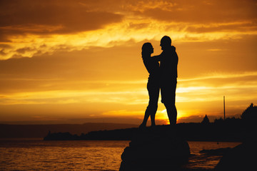 Silhouettes of a couple in love kiss at sunset by the sea