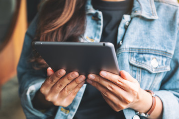 Closeup image of a woman holding and using tablet pc while sitting in cafe