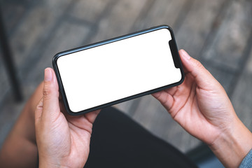 Top view mockup image of a woman holding a black mobile phone with blank white desktop screen