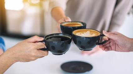 Closeup image of people enjoyed drinking and clinking coffee cups on the table in cafe