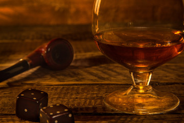 Glass with cognac or whiskey and smoking pipe on a wooden table. Dark and Moody style.