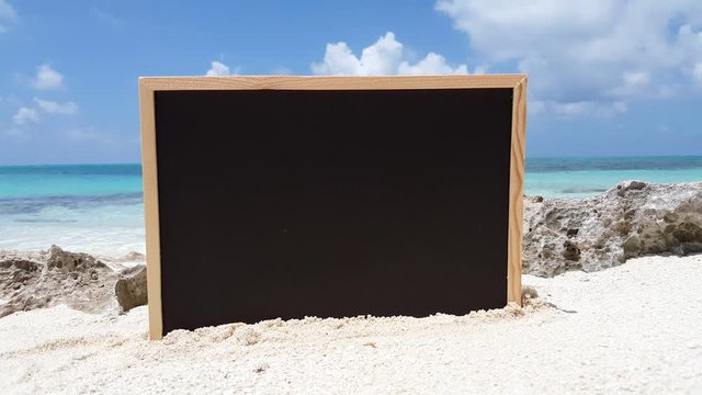 Empty blackboard plunged on white sandy grains ready for writing on a blur background of sea and sky, concept design