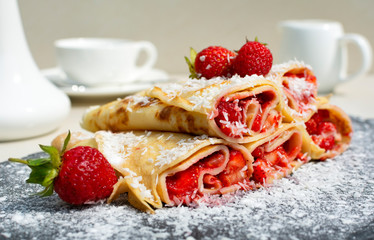 Rolled crepes or balkan pancakes stuffed fresh chopped strawberries, decorated powdered sugar and coconut flakes . Gourmet sweet dish