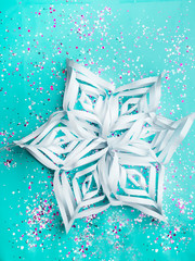 Snowflake from paper with colorful confetti on trendy mint colored background. Simple holiday concept. Winter festive backdrop. Top view, flat lay, copy space