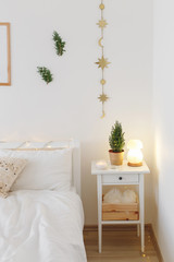 Little christmas tree in a pot and night salt lamp on bedside table. New year winter home interior decor. Christmas holiday decorations with led garland lights. White stylish cozy scandinavian bedroom