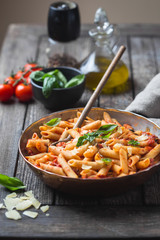Penne pasta in tomato sauce and cheese decorated with basil on a wooden background