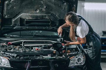 Fototapeta na wymiar Beautiful Mechanic girl in a black jumpsuit and a white T-shirt changes the oil in a black car. car repair concept
