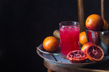 Glass of blood orange juice with ice and orange fruits on dark background