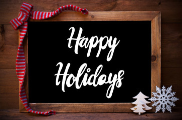 Fototapeta na wymiar Chalkboard With English Calligraphy Happy Holidays. Christmas Decoration Like Tree, Snowflake And Bow. Wooden Background