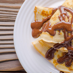 Flat lay French crepes with chocolate sauce in ceramic dish on wooden kitchen table