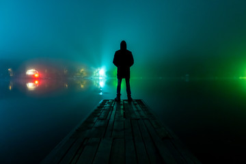 silhouette of a man and a lake in the fog at night