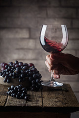 Red wine glass in a men hand and ripe grapes on wooden background