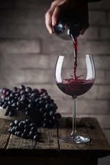 Keuken foto achterwand Pouring red wine into the glass against wooden background © petrrgoskov