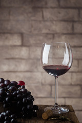 Red wine in a glass and ripe grapes on wooden table