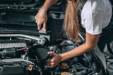 Beautiful Mechanic  girl in a black jumpsuit and a white T-shirt changes the oil in a black car.close up photo. car repair concept