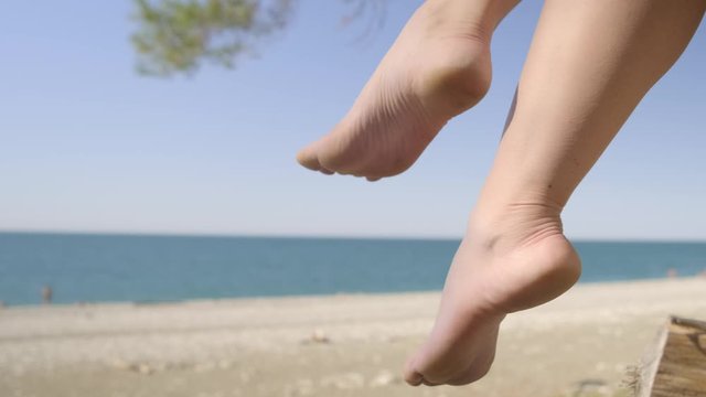 Female legs swing against backdrop of sea beach. Woman shakes legs on background of sea beach.
