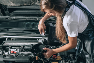 Obraz na płótnie Canvas Beautiful Mechanic girl in a black jumpsuit and a white T-shirt changes the oil in a black car.close up photo. car repair concept