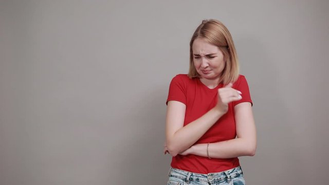 Portrait of confused young woman looking aside and covering nose with hand isolated on grey wall background in studio. People sincere emotions, lifestyle concept.