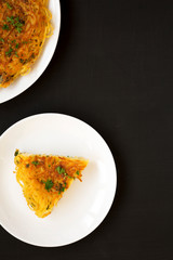 Homemade spaghetti omelette on a white plate over black background, top view. Flat lay, overhead, from above. Copy space.