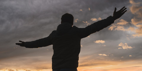 Man standing with his arms wide open under an evening sky