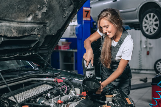 Beautiful Mechanic  girl in a black jumpsuit and a white T-shirt changes the oil in a black car. car repair concept