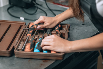 female hands with pink manicure and brown case with screwdrivers in the garage