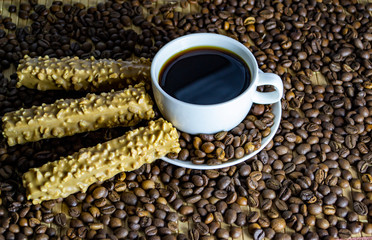 a cup of coffee with cookies, coffee grains scattered on a table near a cup with a coffee