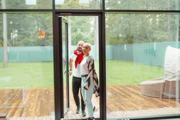 Attractive family couple entering new house, happy to spend time here. Background big panoramic window