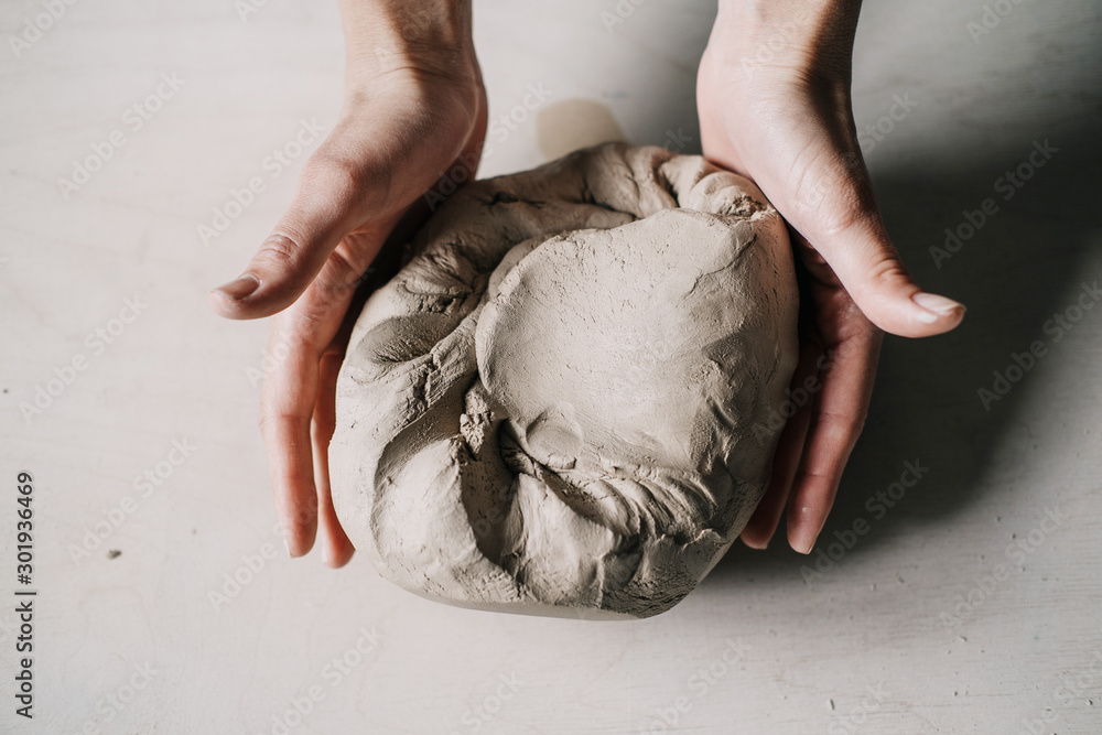 Wall mural female potter hands working with clay in workshop. white desk on background