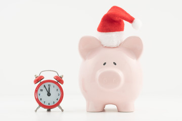 Pink piggy bank wearing a Santa hat standing alongside a red alarm clock.