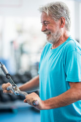 one mature man lifting a weight with a machine at the gym - active senior training hard alone - healthy and fitness man