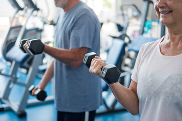 couple of two seniors and mature people at the gym doing exercise - adults holding a dumbbell and working biceps together