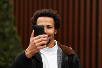 Young American guy holds smartphone in his hand, covering his face. Digital Generation Addiction concept.