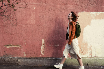 Young female wearing little backpack walking outdoor in city opposite coloured wall