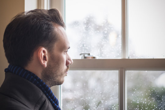 Portrait of a man looking out window during cold winter