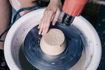 Female potter hands working with clay in workshop. White desk on background