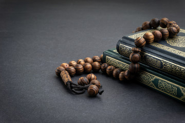 Holy Quran with arabic calligraphy meaning of Al Quran and tasbih or rosary beads on black...