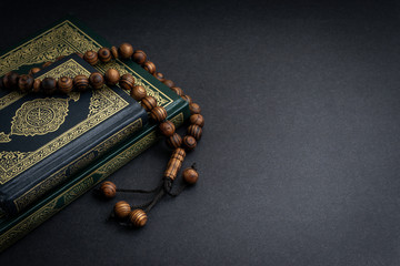 Holy Quran with arabic calligraphy meaning of Al Quran and tasbih or rosary beads on black...