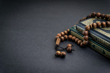 Holy Quran with arabic calligraphy meaning of Al Quran and tasbih or rosary beads on black...