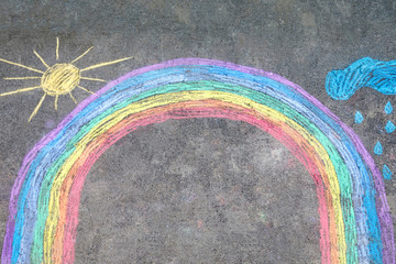 Rainbow sun and clouds with rain drops painted with colorful chalks on ground or asphalt in summer....