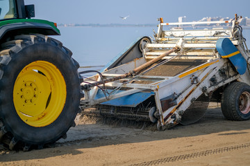Tractor cleaning sand in the beach on blue sea background. Beach garbage cleaning machine at work....
