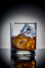glass of whiskey with ice on a glass surface
