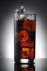 glass of cola with ice on a glass surface