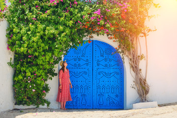 Girl next to home entwined liana with flowers in Sidi Bou Said, Tunisia