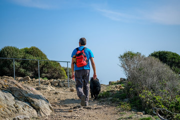 A man with a dog walking in the mountains of Catalonia on blue sky background. A man travels on a tourist route, a mountain path. Healthy, active lifestyle at any age. Walking trails, hiking.