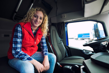 Truck driver occupation. Female trucker sitting in truck cabin and smiling. Woman at work....