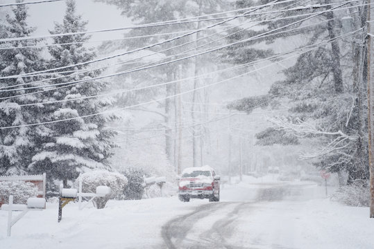 Winter street view during snowfall. Coniferous trees in the snow and a car covered with snow. USA. Maine